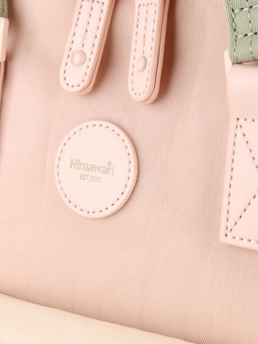 Close-up of the Himawari backpack's round logo and pink straps, emphasizing its brand detail and stylish craftsmanship.