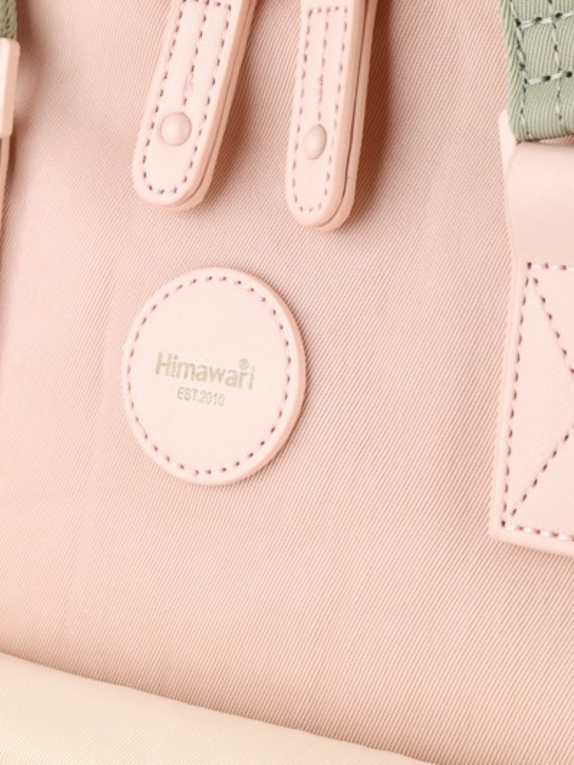 Close-up of the Himawari backpack's round logo and pink straps, emphasizing its brand detail and stylish craftsmanship.
