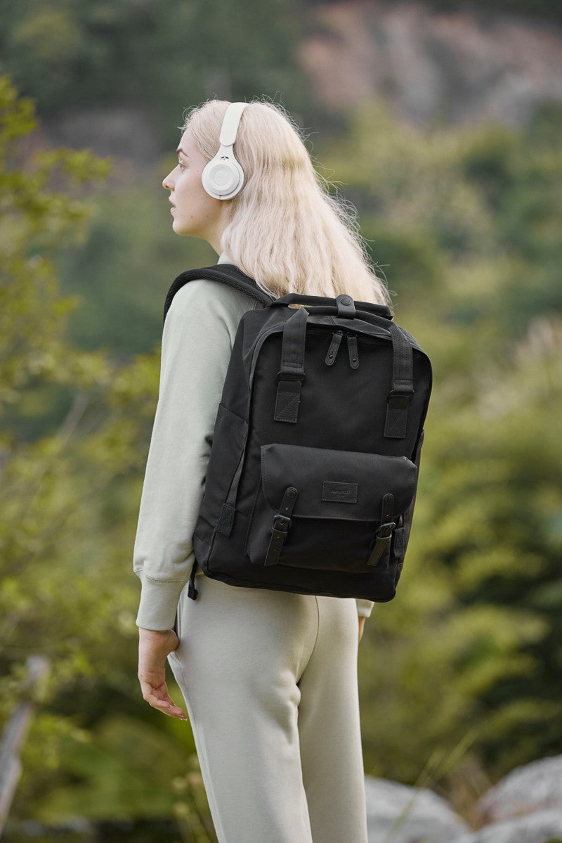 Person wearing a black Himawari waterproof canvas backpack in a natural outdoor setting, ideal for travel and casual use.